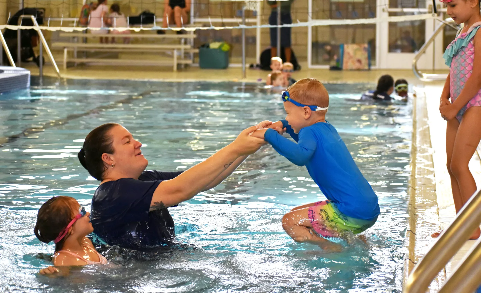 Swim lesson instructor helping child jump into pool