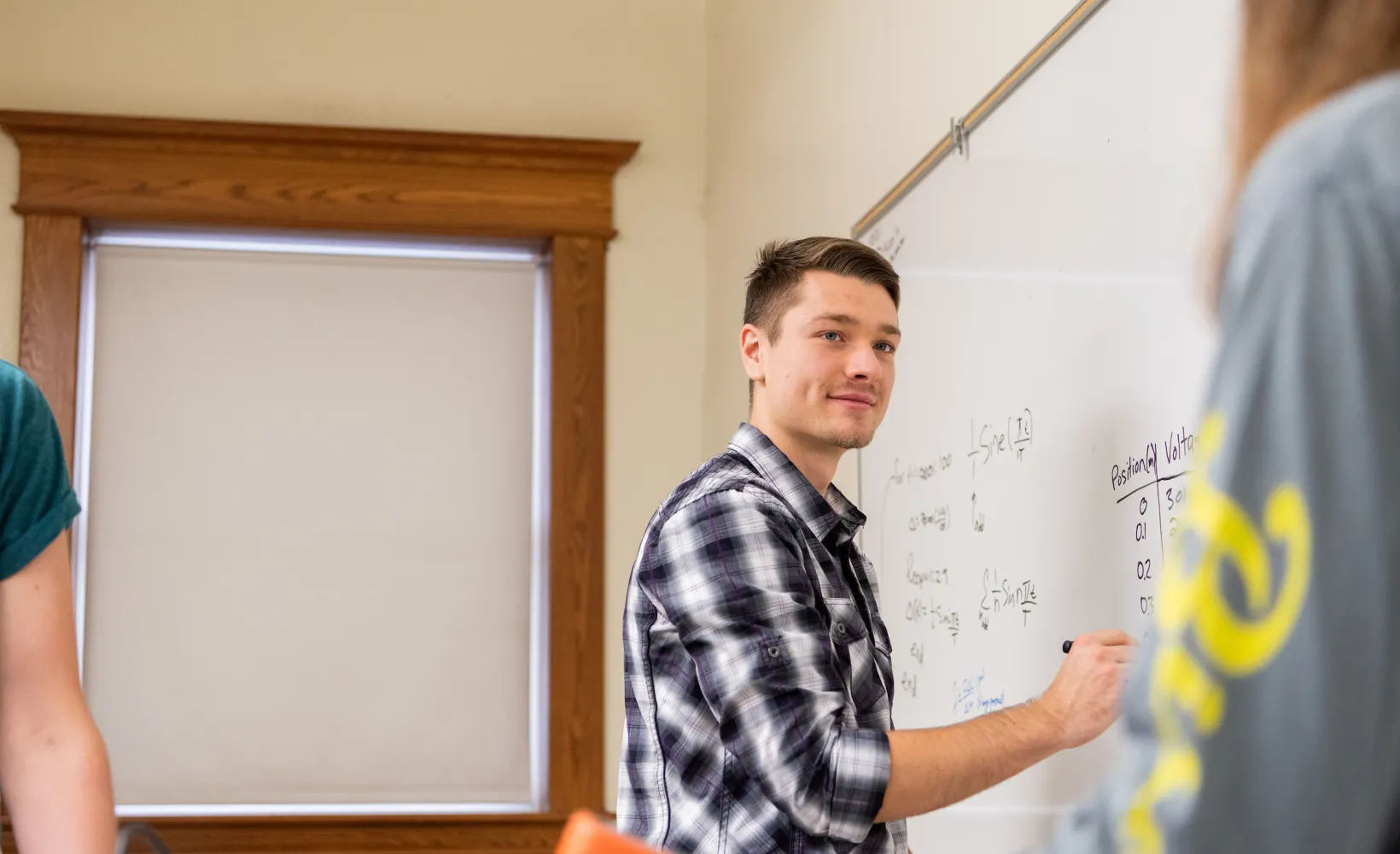 students discuss as one writes on a whiteboard 