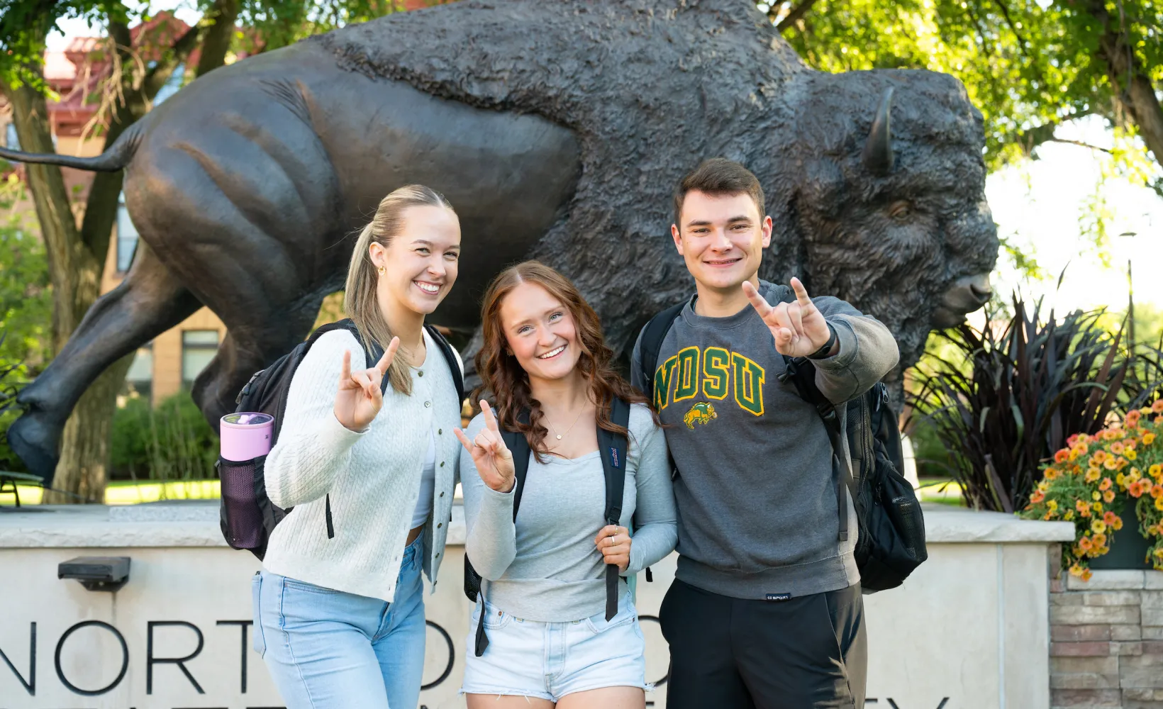 The people stand in front of a Bison statue