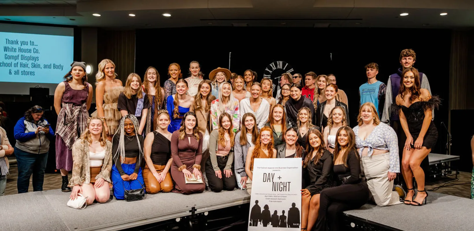 Large group of students posing on stage at fashion show.