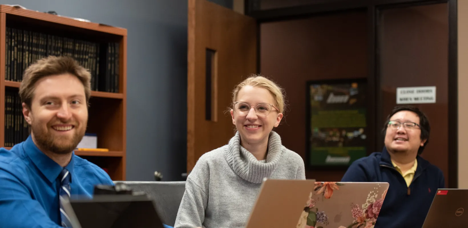 Student sitting at table with other students smiling confidently at the front of room. 