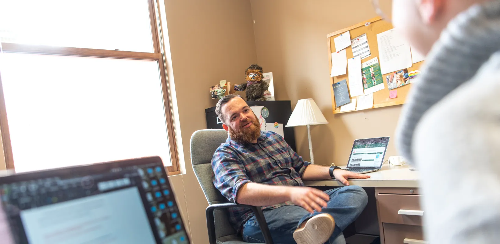 Student lounging at desk while talking with another student.