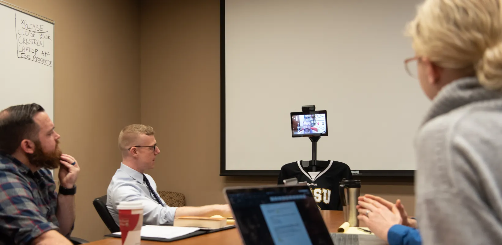 Four people participating in a zoom meeting with one person online.