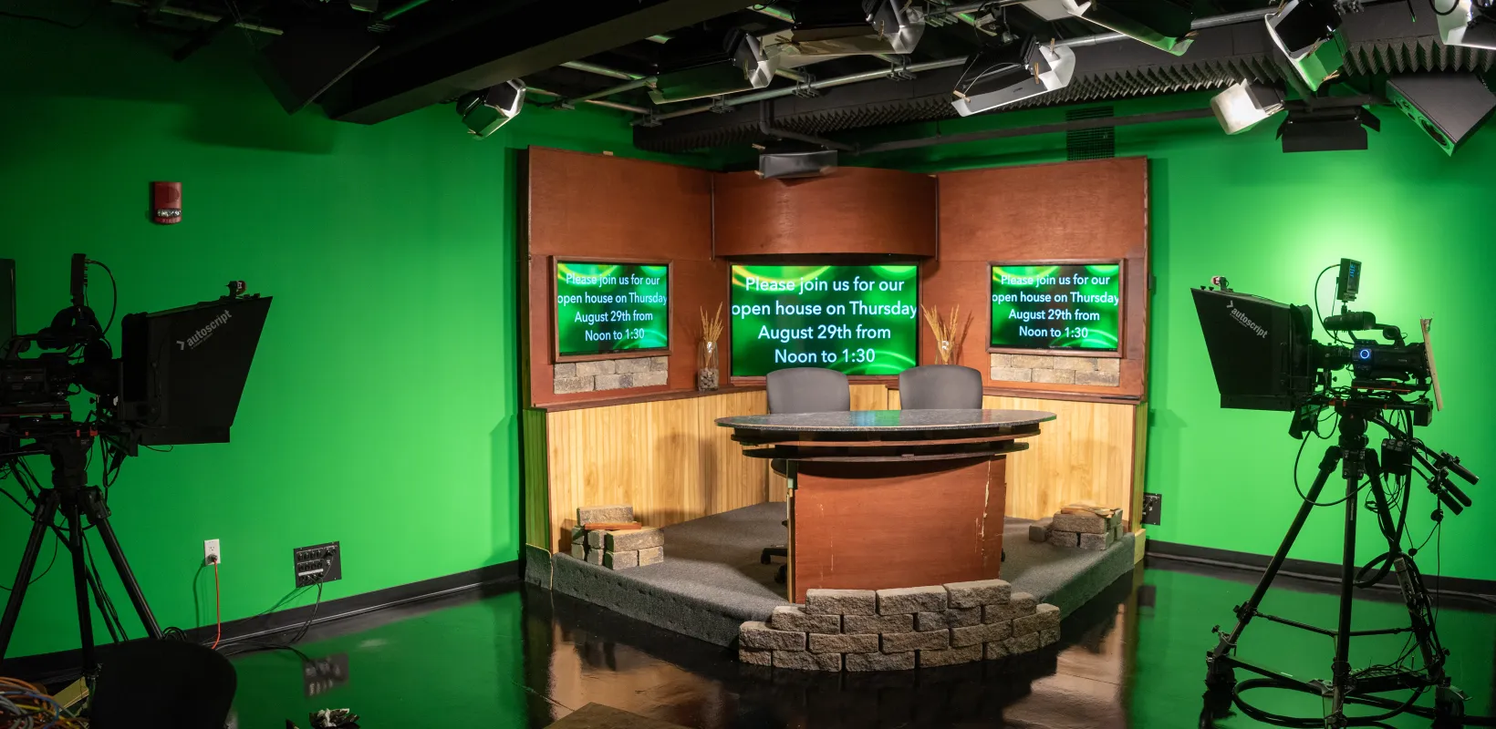 Bison Information Network studio with cameras pointed at desk with 2 chairs and screens located behind desk.