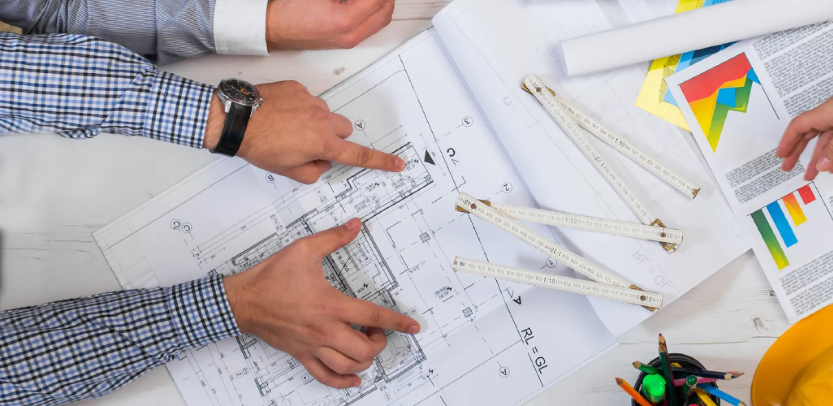 Project Team Members all working on a project with all pointing to papers on a table with a hardhat, and computer