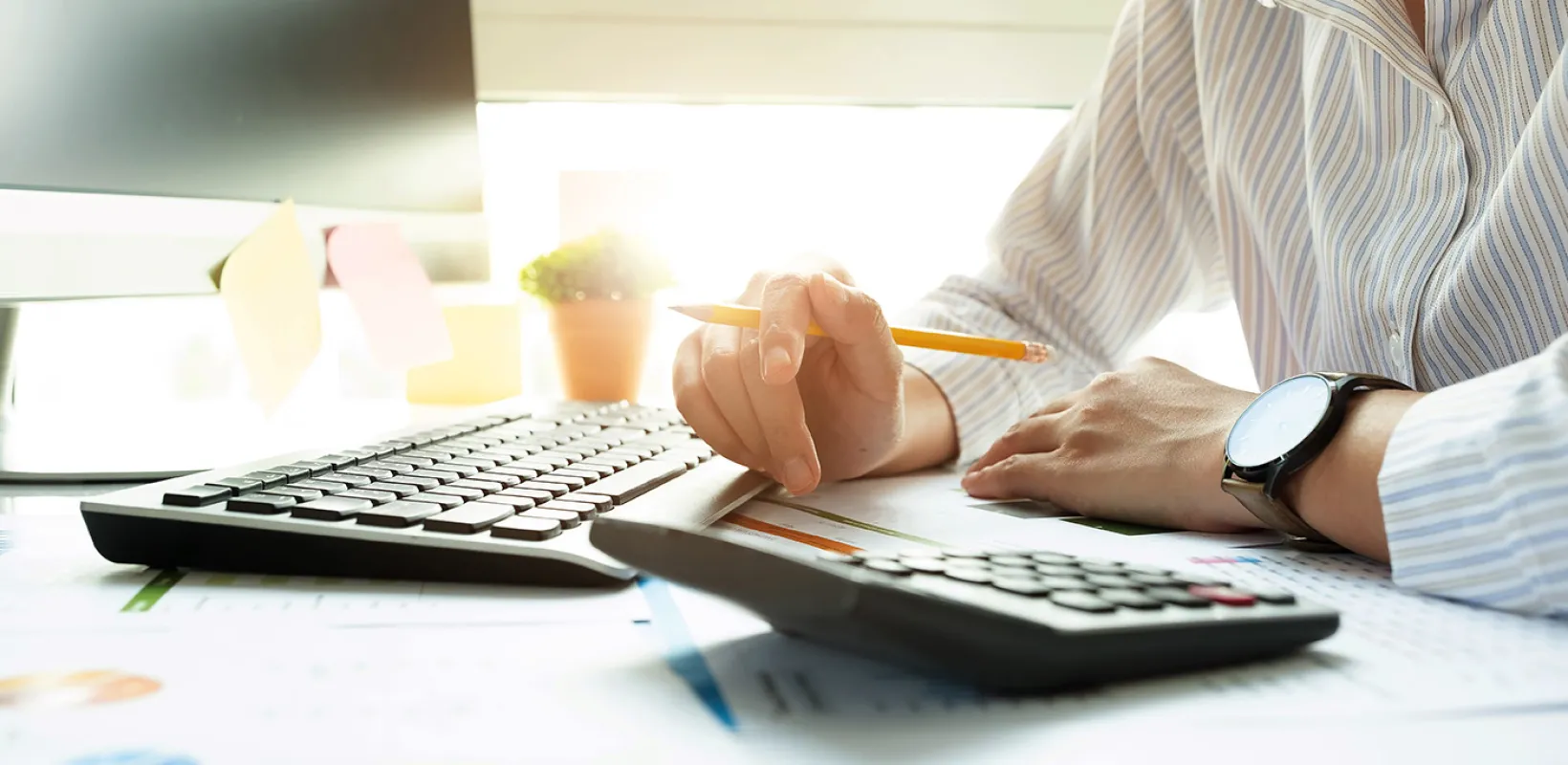 Bookkeeper arm resting on document with a pencil, calculator and keyboard