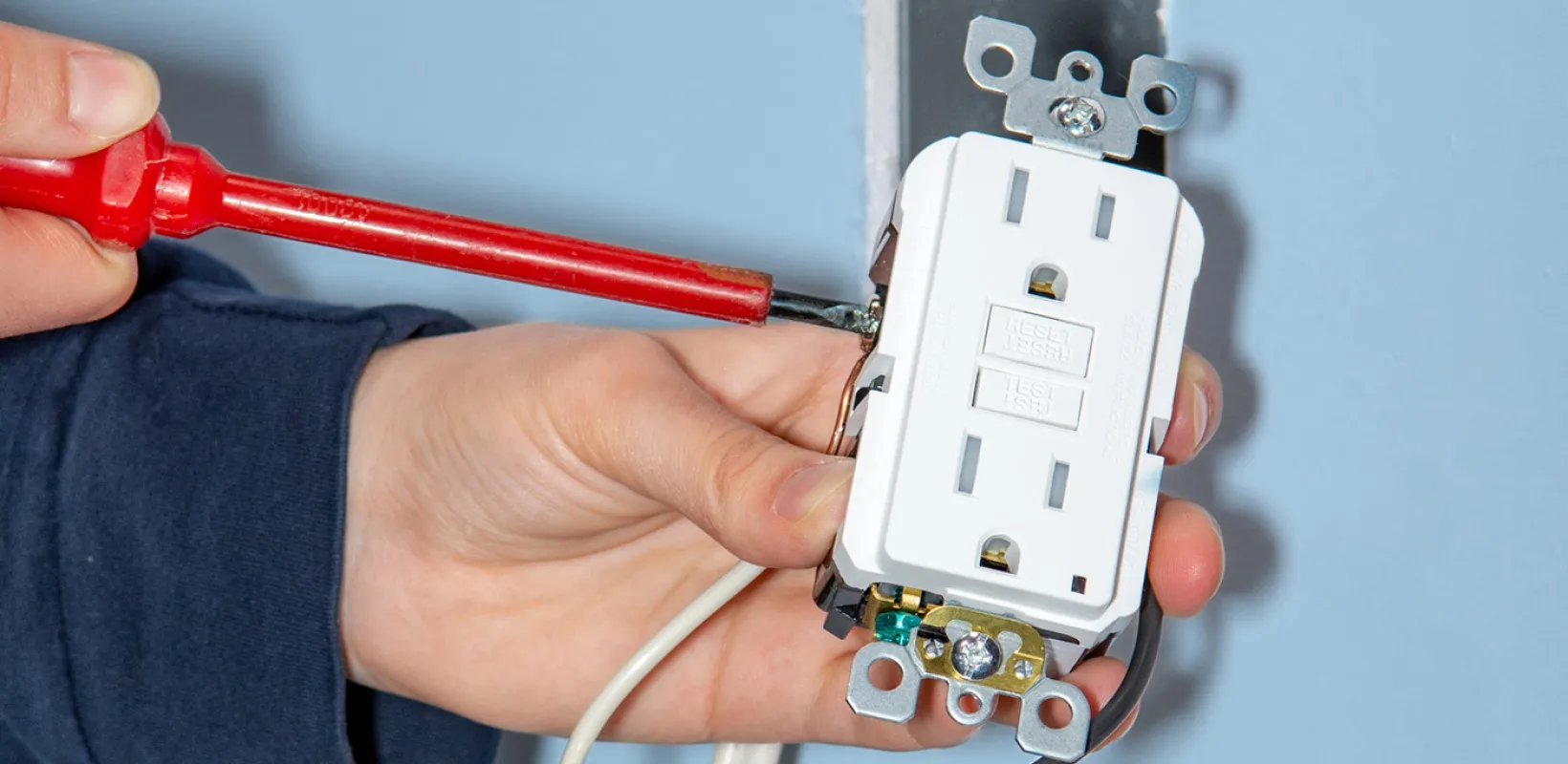 Electrician with a screwdriver working on an electrical outlet