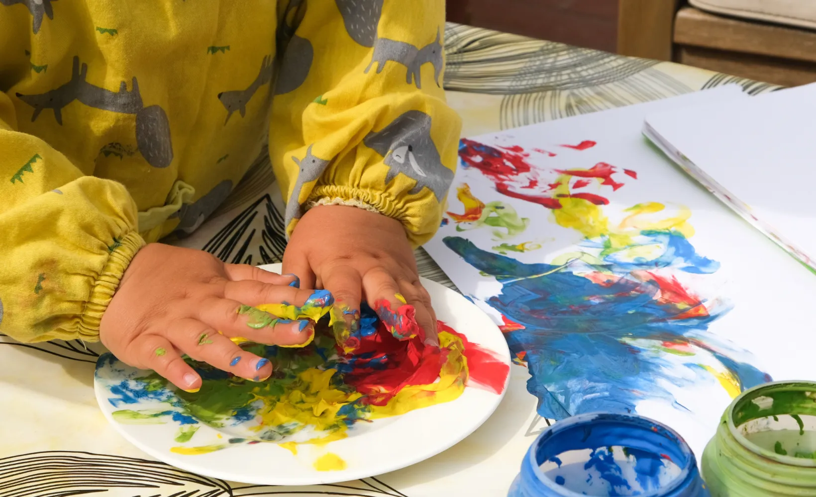 A child wearing a yellow long-sleeved shirt working with finger paint and white paper.