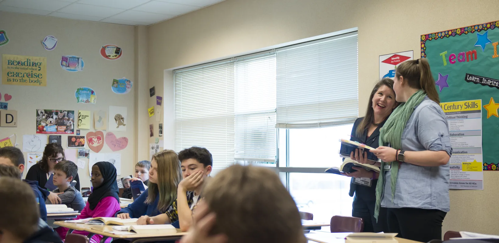 Teacher talking with a student teacher in a classroom setting with students sitting at individual desks