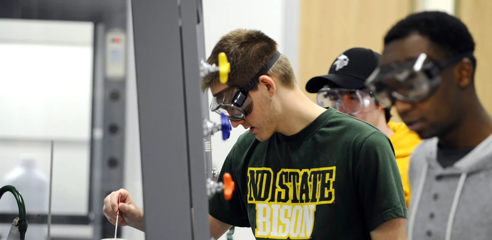 Student working in lab wearing goggles and a green NDSU Bison t-shirt