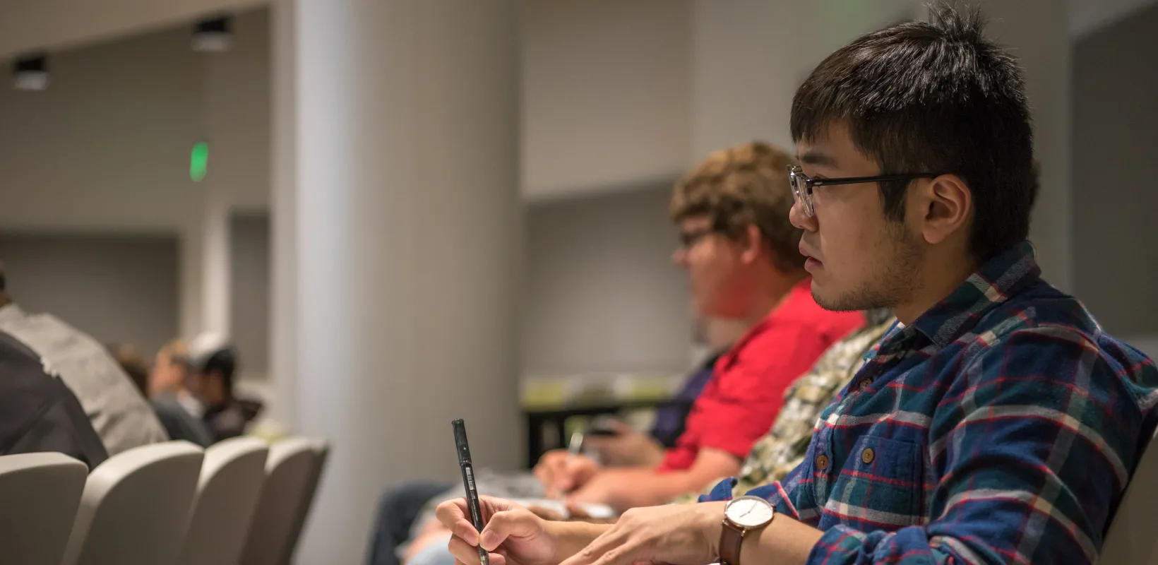 Student sitting in Trig class looking intently at the front of room while holding a pen just above his paper.