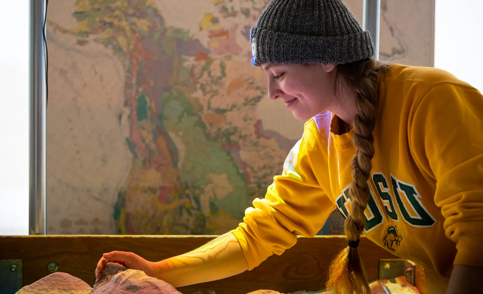 Student wearing a yellow NDSU sweatshirt working in AR sandbox.