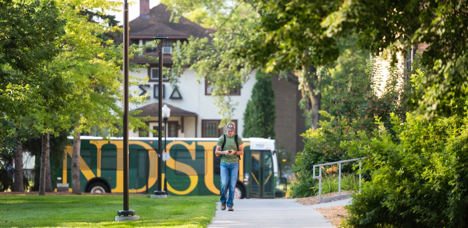 Student walking on campus, looking at phone. 