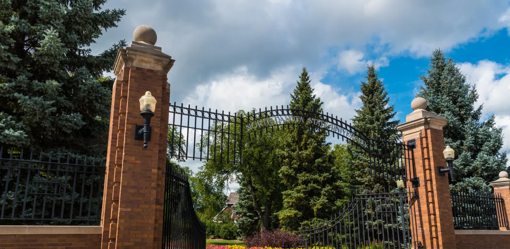 NDSU Gate surrounded by yellow and pink flowers.