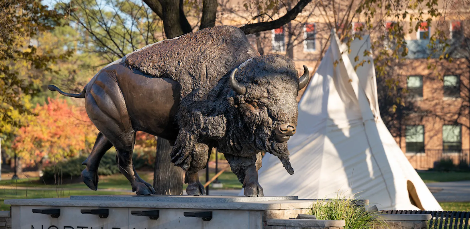 Bronze Bison statue with teepee in the background.