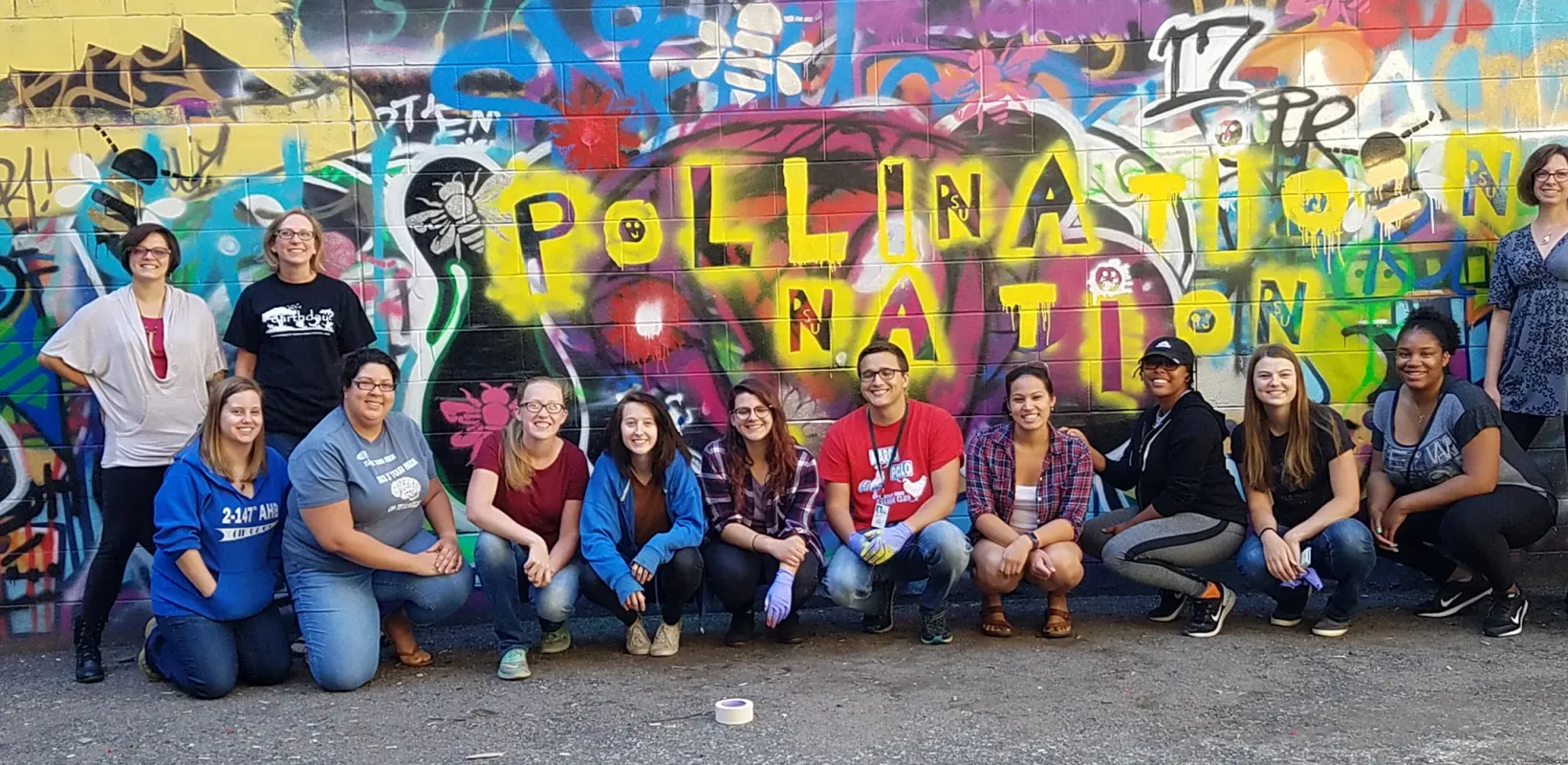 Pollination Nation research students smiling confidently at camera in front of a colorful graffiti wall.