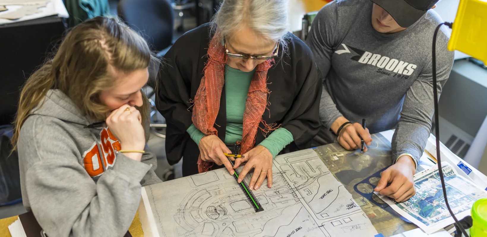 Faculty teaching two students using a ruler and a drawing on paper.