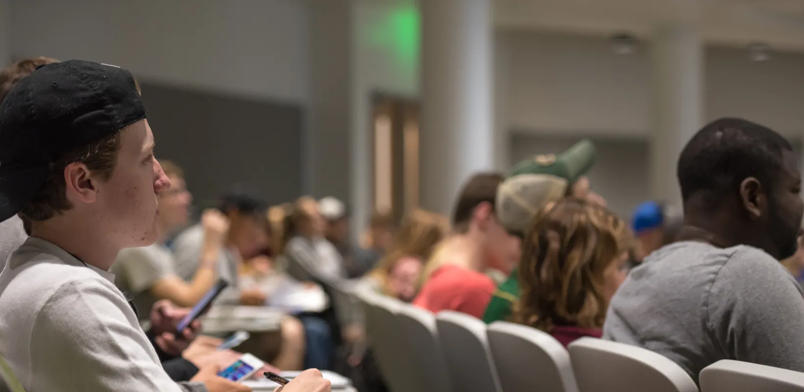 Student sitting in a lecture classroom setting with pen and paper on desktop.