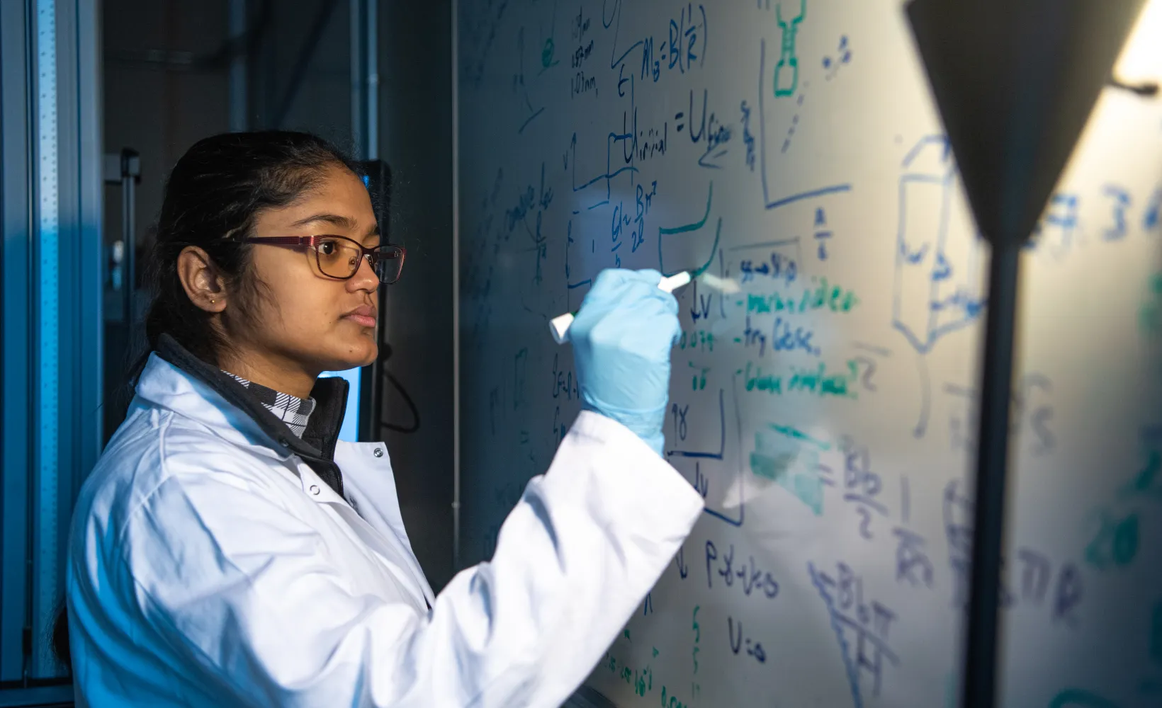 Research student working at a whiteboard, looking intently at what she is currently writing.
