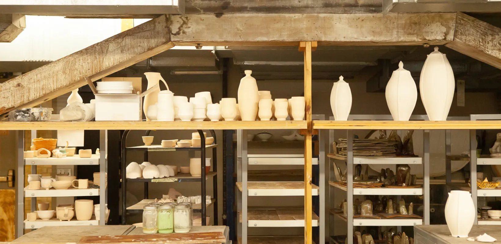 Shelves with dried clay pots of all shapes and sizes, tables and equipment in ceramics studio.