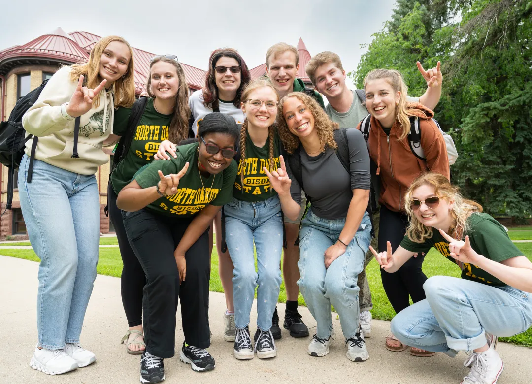 students posing in front of Old Main and giving Bison horns