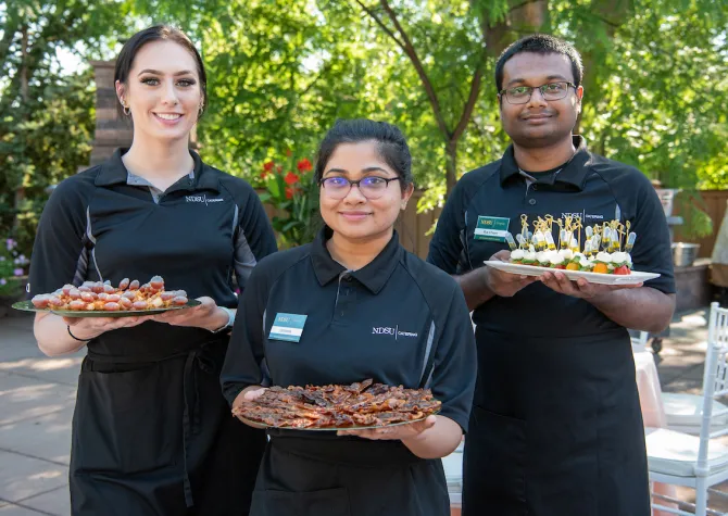 Three NDSU Catering employees holding trays of appetizers