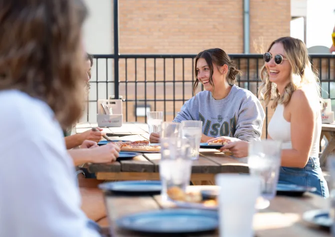 Students laughing and eating pizza on a rooftop