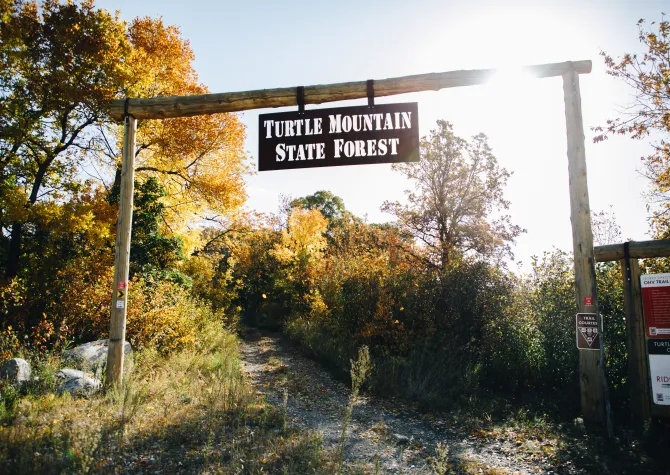 A sign that reads "Turtle Mountain State Forest" hung in front of a nature trail