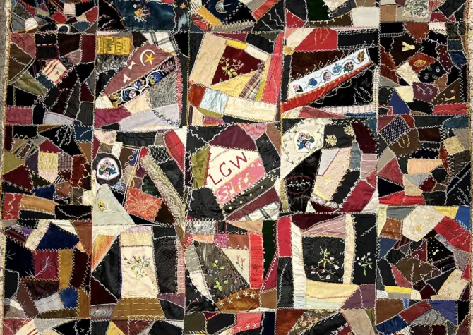 Quilt with many different colors shapes and sizes of fabric sewn together.