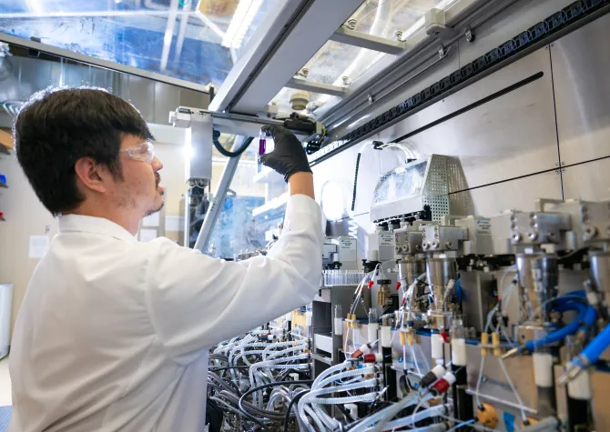 Research student wearing a white lab coat and black gloves while working in the lab.