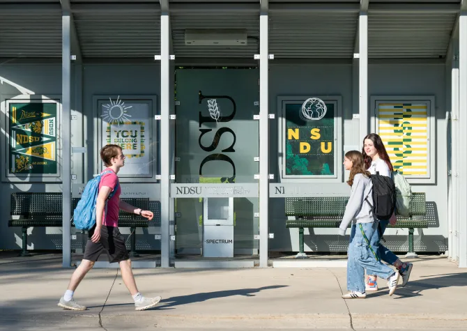 three students walking in front of bus stop on campus