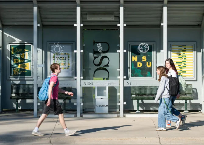 three students walking in front of bus stop on campus