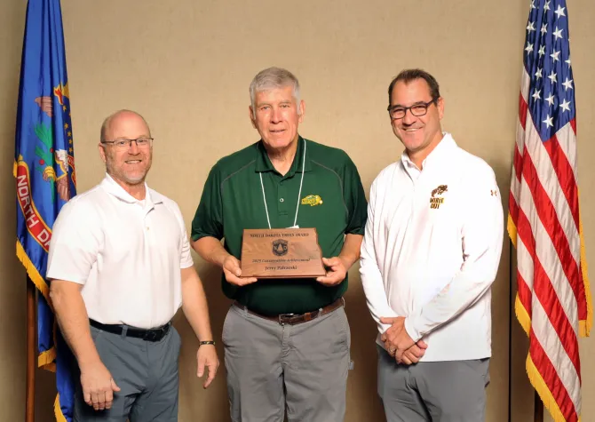 A man holds a plaque next to two men smiling
