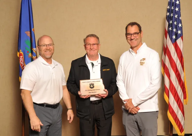 A man holds a plaque next to two men smiling