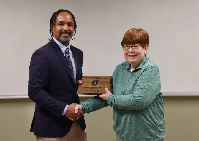An African American man hands a plaque to a woman and shakes her hand