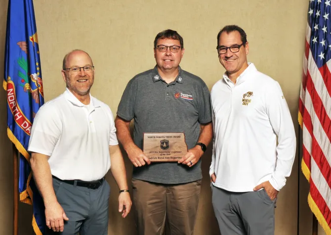 A man holds a plaque next to two men smiling