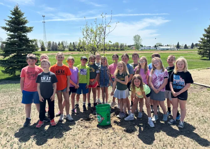 A group of kids smile after planting a tree