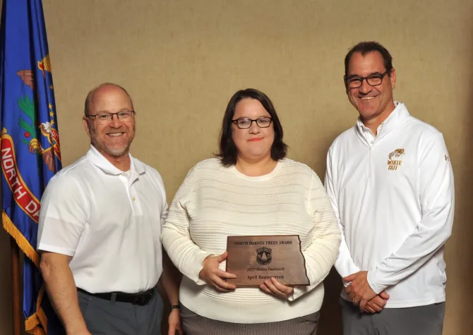 A woman holds a plaque next to two men smiling