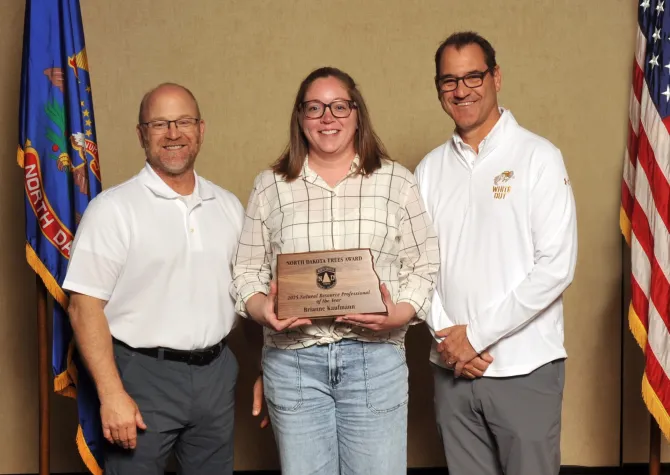 A woman holds a plaque next to two men smiling