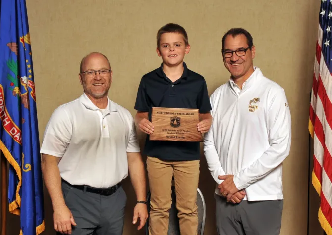 A noy holds a plaque next to two men smiling