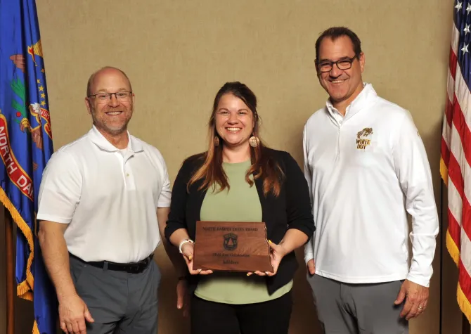 A woman holds a plaque next to two men smiling