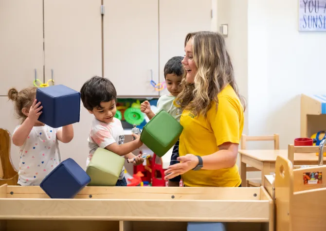 children in wellness center child care playing with colorful foam blocks laughing with student teacher