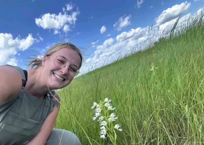 Trinity Atkins smiling at camera will sitting in a green grassy field. 
