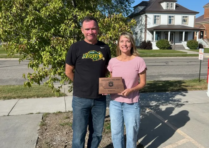 A man stands next to a woman who is holding a North Dakota shaped plaque