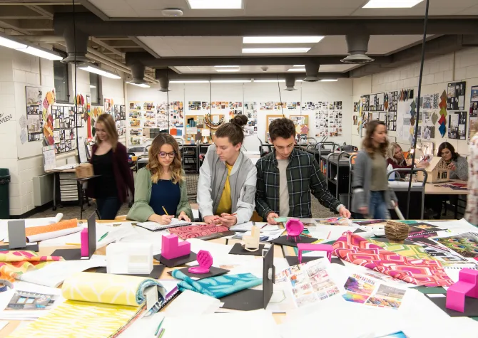 Design students working together with fabric samples and miniature models in the design studio.