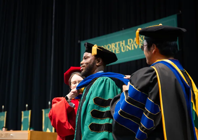 graduate receiving his commencement regalia during the ceremony