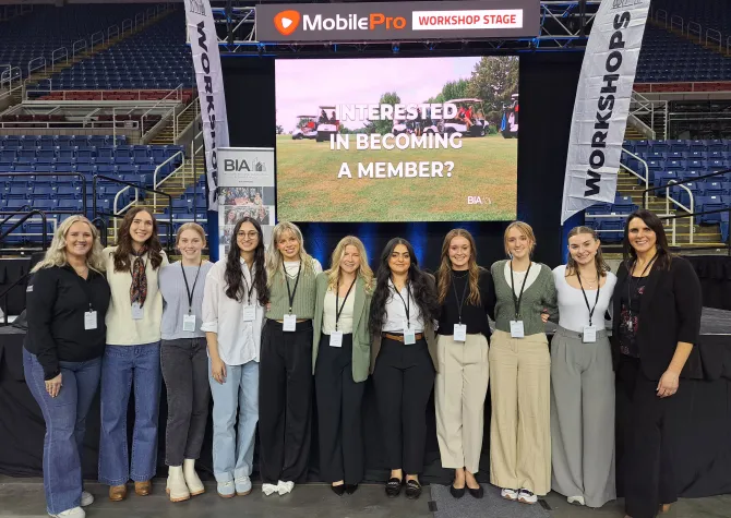 A group of students standing in front of screen smiling confidently at camera.