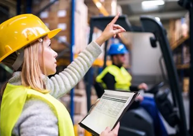 Woman manager in hardhat looking at a report pointing at a pallet