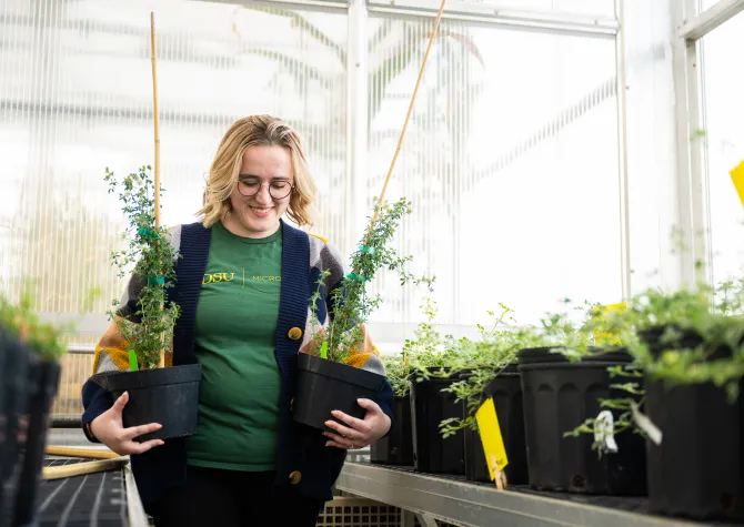 Microbiology grad student holding plants in greenhouse
