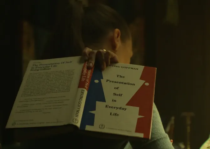 Woman looking down and off camera holding The Presentation of Self in Everyday Life by Erving Goffman
